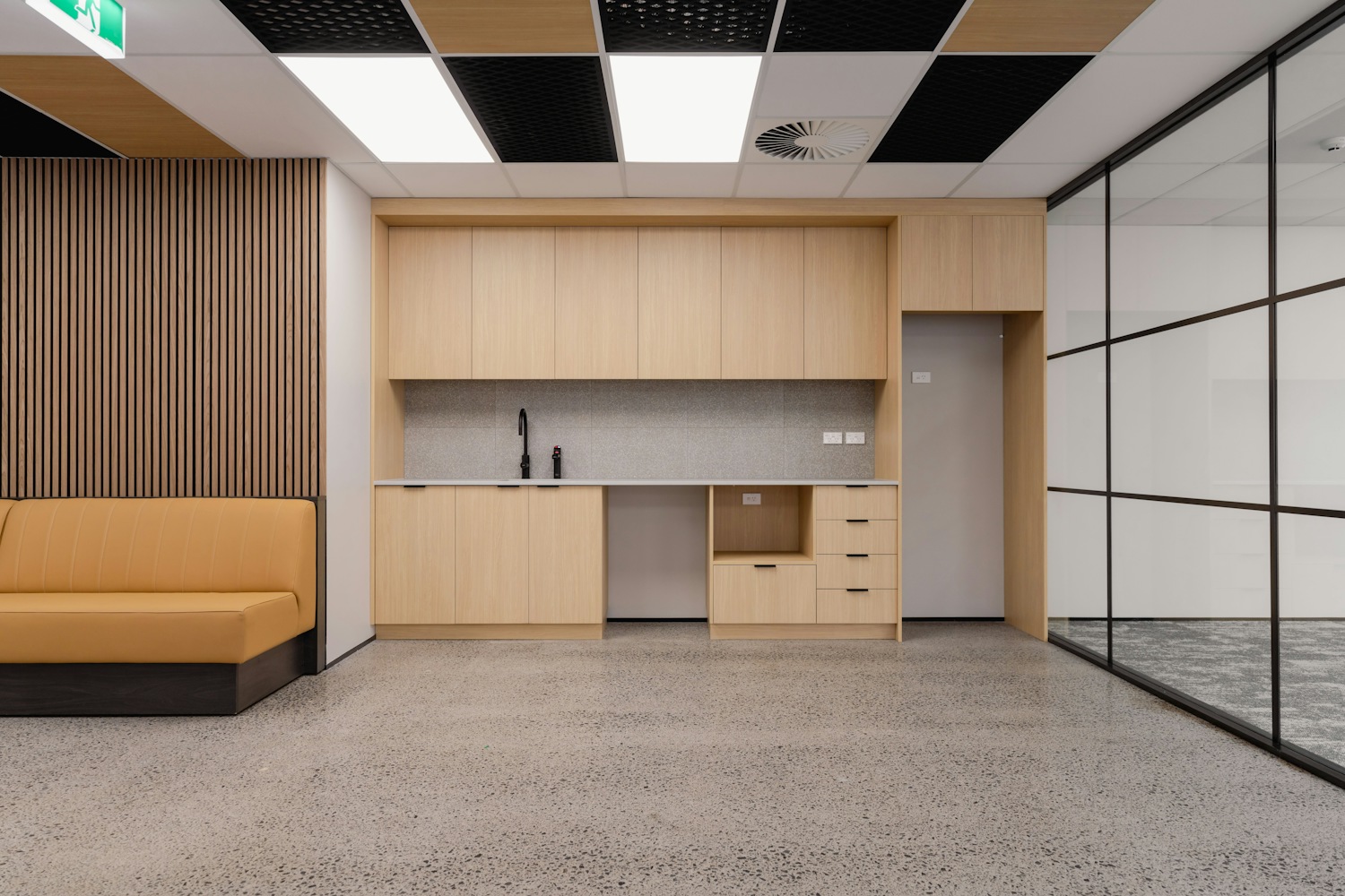 Modern office kitchenette with wooden cabinets and sofa